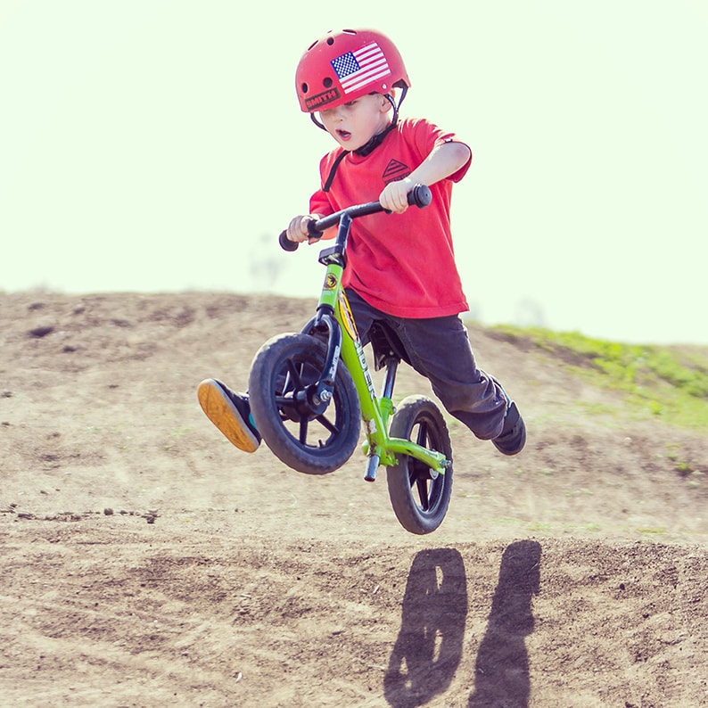 Kid with Strider Balance Bike on terrain with woops